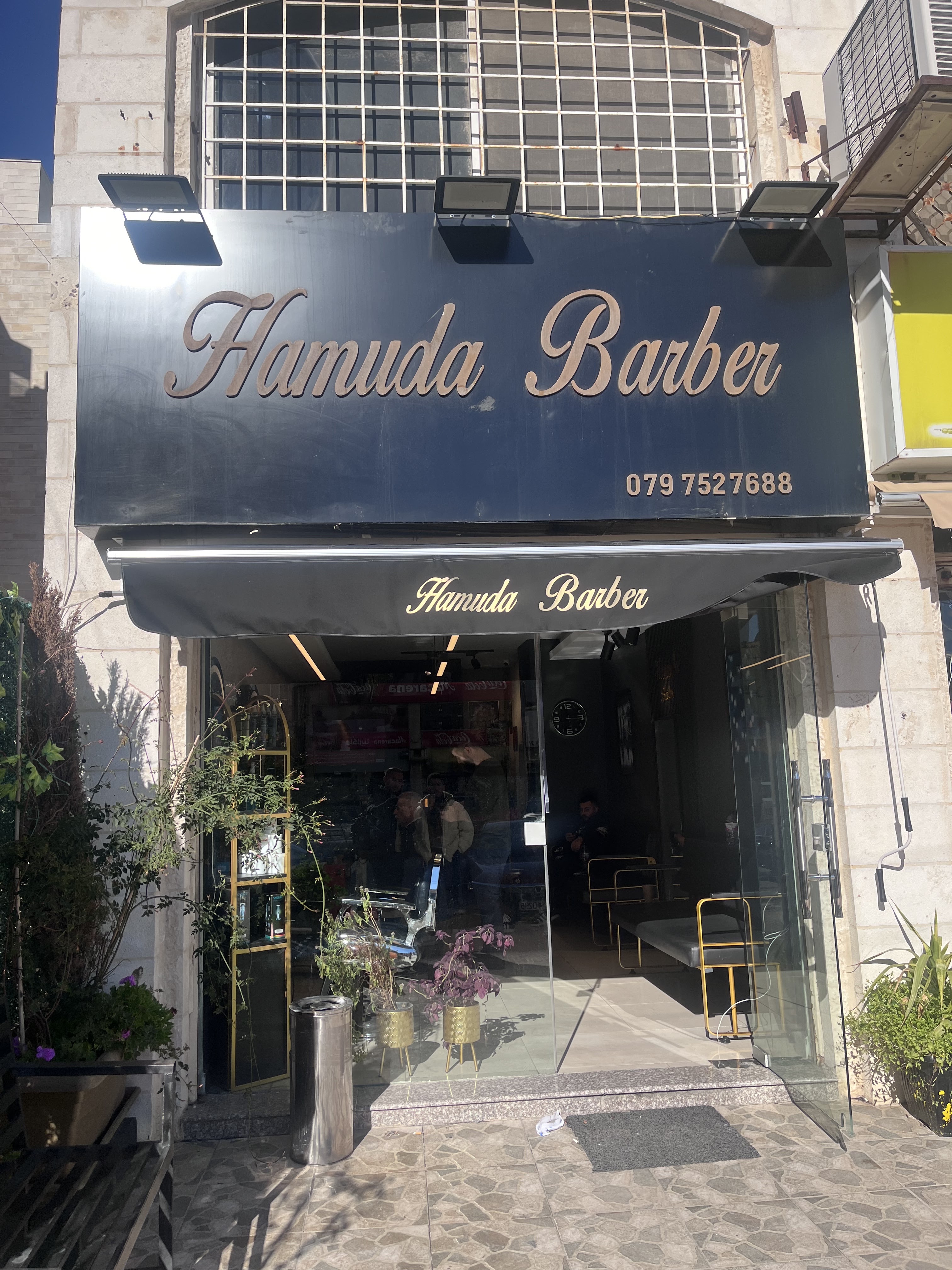 Hamuda Barber storefront on Abdullah Al-Azab St. in daylight, with the shop sign and phone number